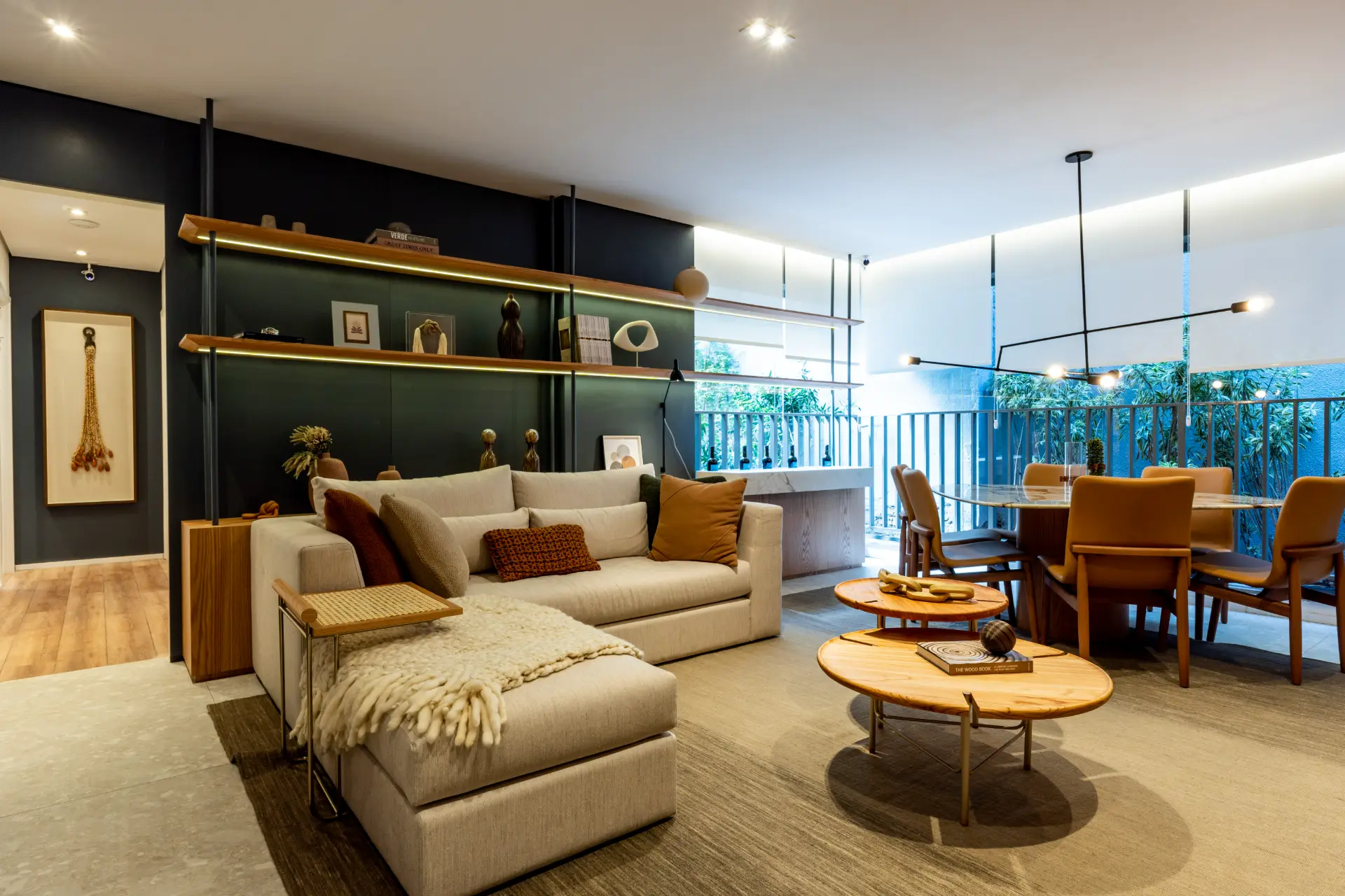 Sala do apartamento decorado de 90 m² com sofá em L, mesas de centro em madeira e varanda verde ao fundo