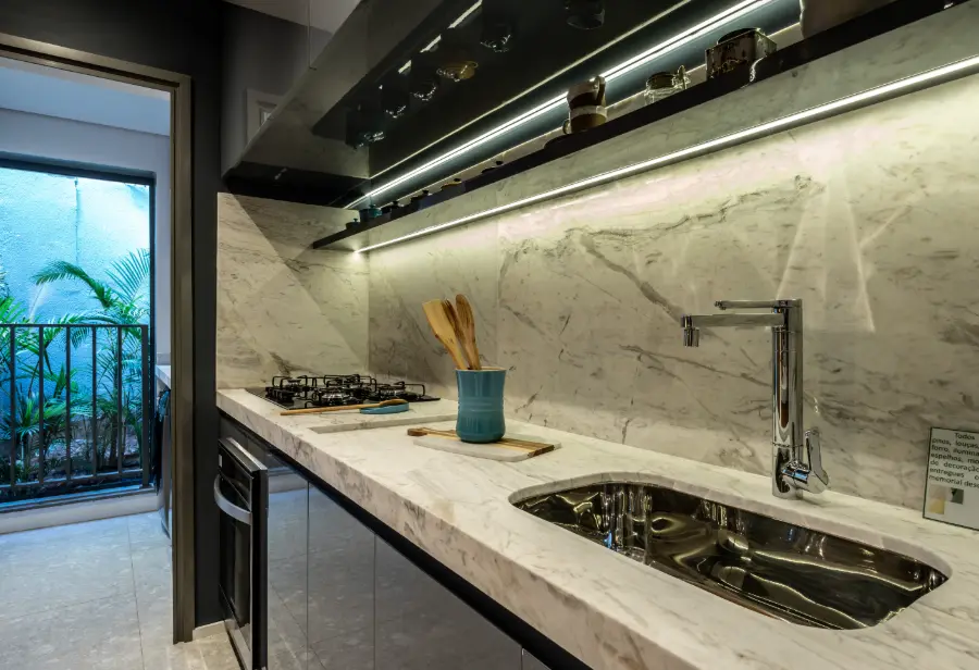 Cozinha do apartamento decorado de 90 m² com bancada de pedra clara, cooktop e luz embutida sob os armários